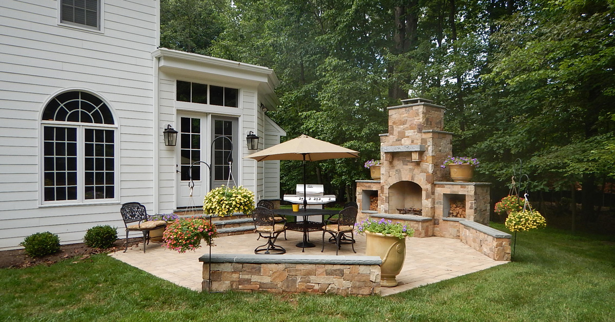 Secluded backyard patio, embellished with rustic stone and a built-in fireplace. It's encased by a serene variety of trees, providing natural privacy and tranquility.
